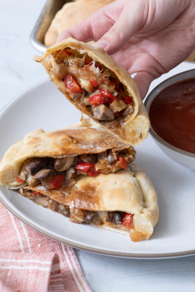 Hand holding Vegetarian Calzone showing vegetable fillings inside.