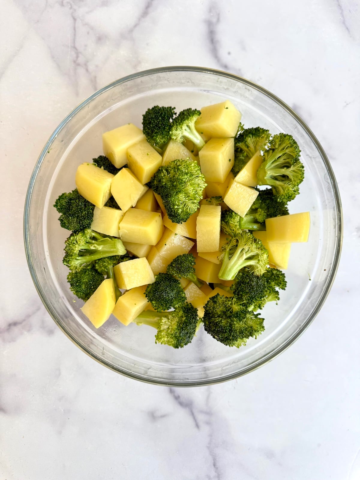 Cubed potatoes and broccoli florets tossed together in a glass bowl.