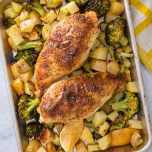 Two za'atar sheet pan chicken breasts roasted with broccoli, potatoes, and lemon on a baking sheet.