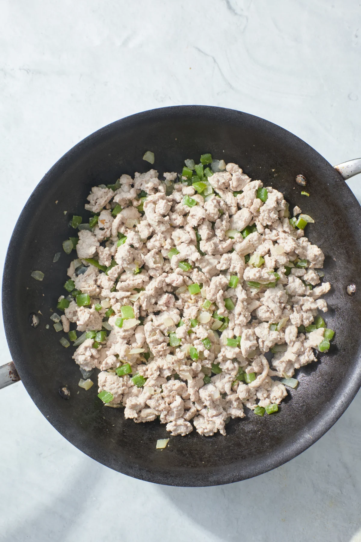 browned ground turkey with sauteed onions, garlic and green bell peppers in pan