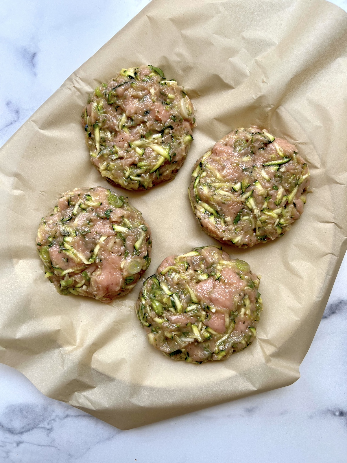 Four turkey zucchini burger patties on parchment paper before being cooked.