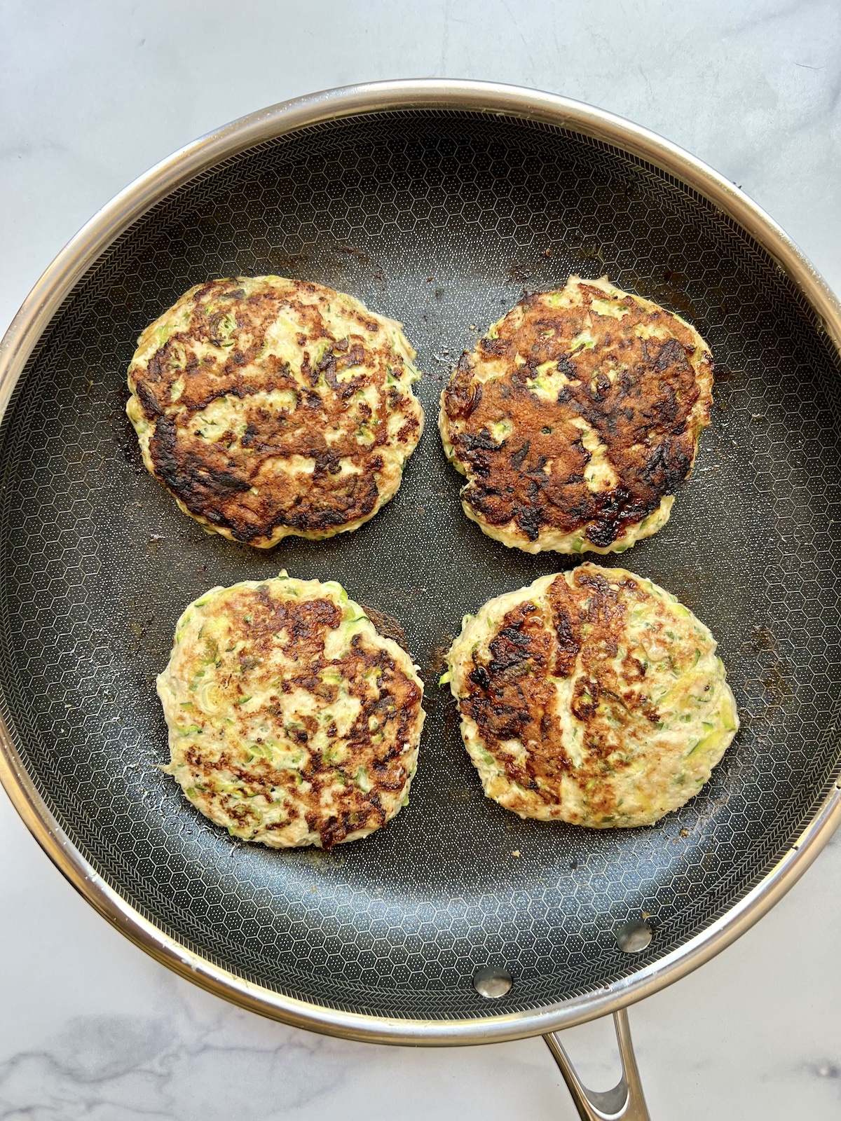 Cooked turkey zucchini burgers on saute pan.