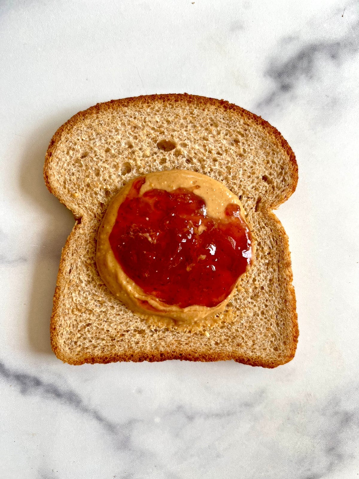Piece of sandwich bread with peanut butter and and fruit preserves in the center.