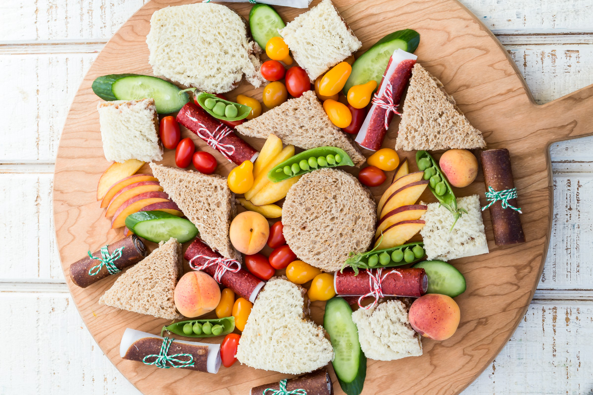 Homemade Uncrustables on large cutting board with fruits and vegetables.