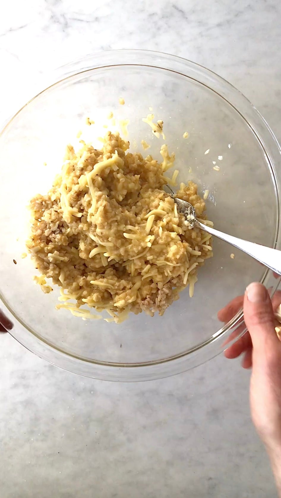 Rice, egg, and shredded mozzarella combined into a cohesive mixture in a glass bowl.