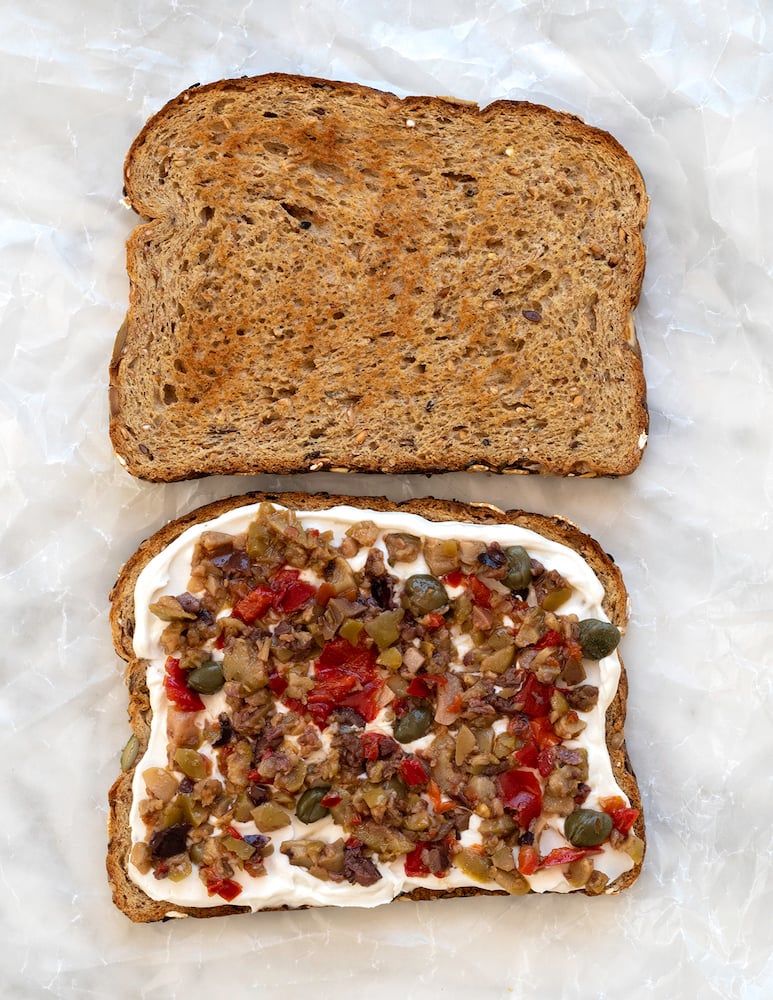 Olive tapenade and cream cheese sandwich on white background.
