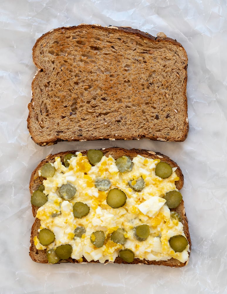 Egg salad with chopped pickles sandwich on white background.