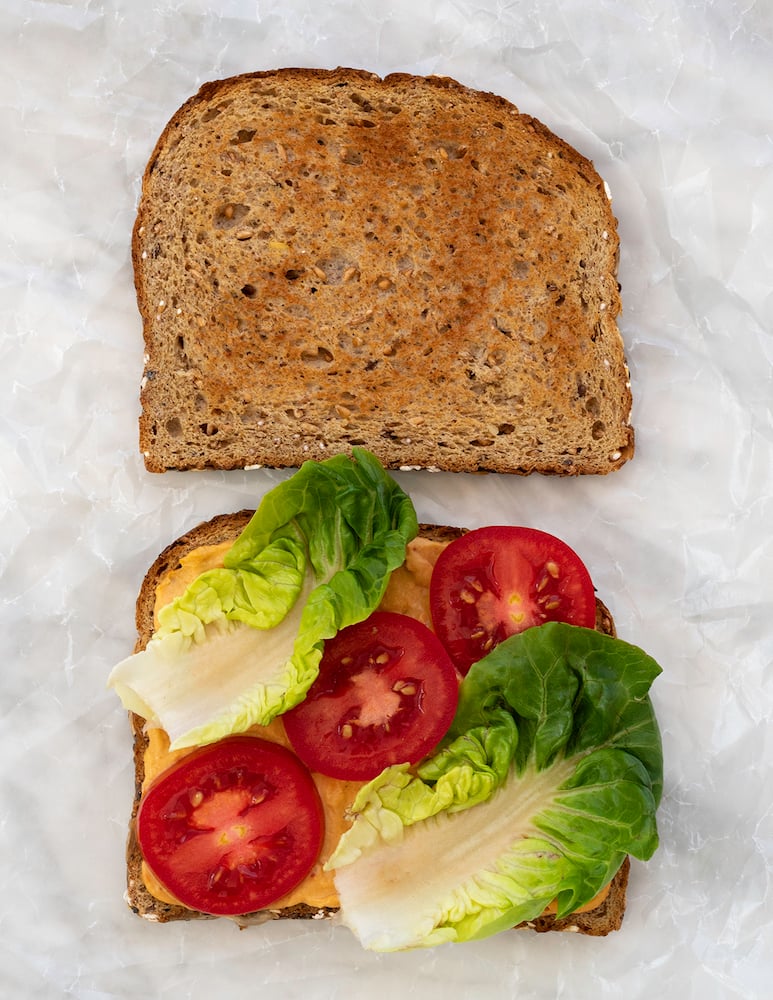 Red bell pepper hummus, lettuce and tomato sandwich on white background.