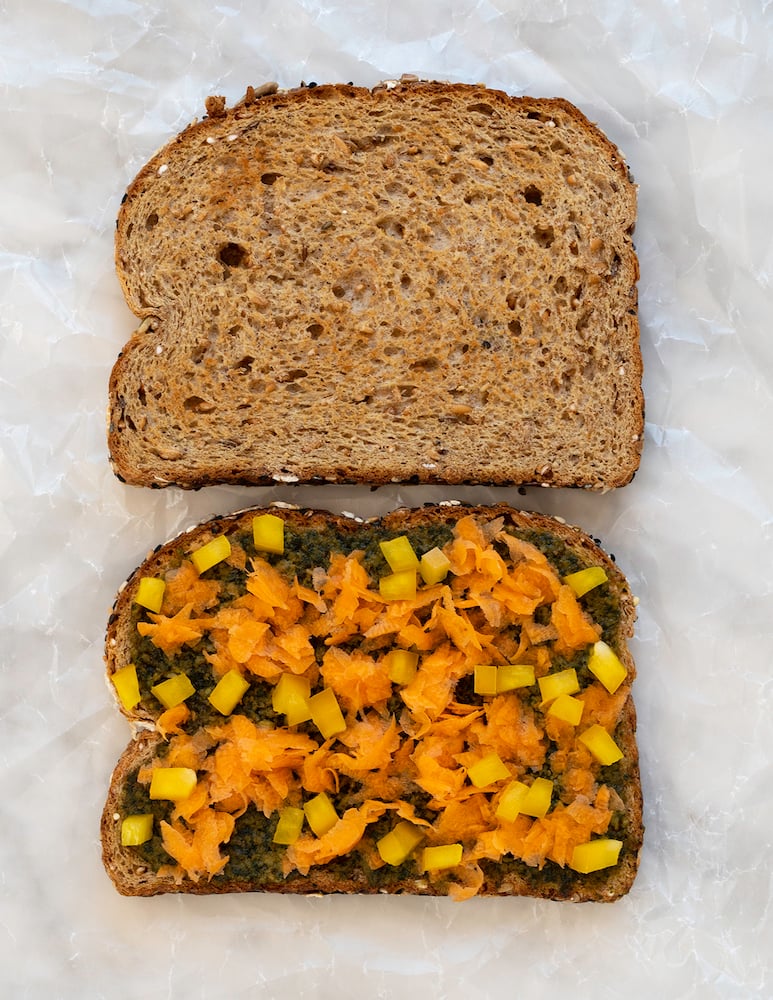 Pesto and chopped veggie sandwich on white background.