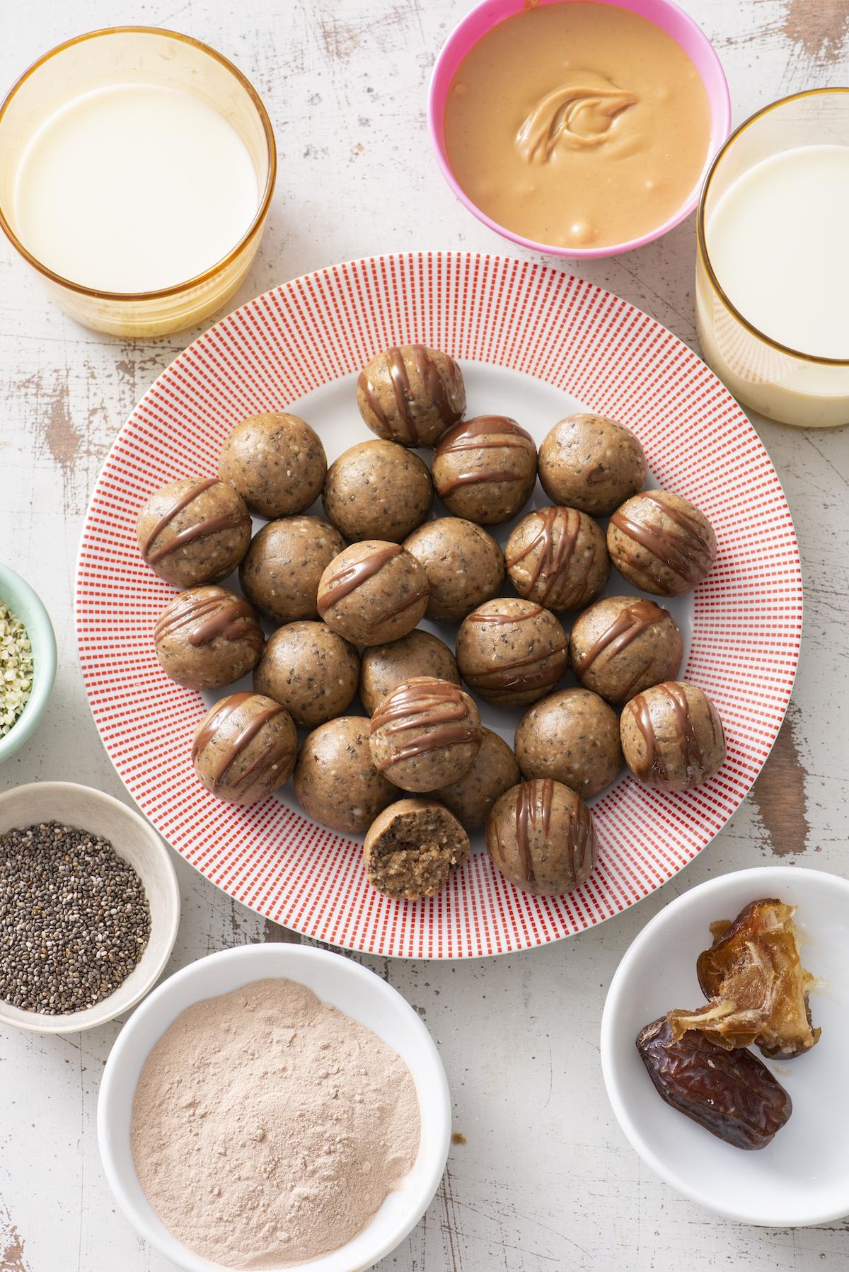 Protein balls on a serving plate surrounded by small dishes with some of the ingredients: dates, peanut butter, chia seeds, and protein powder.