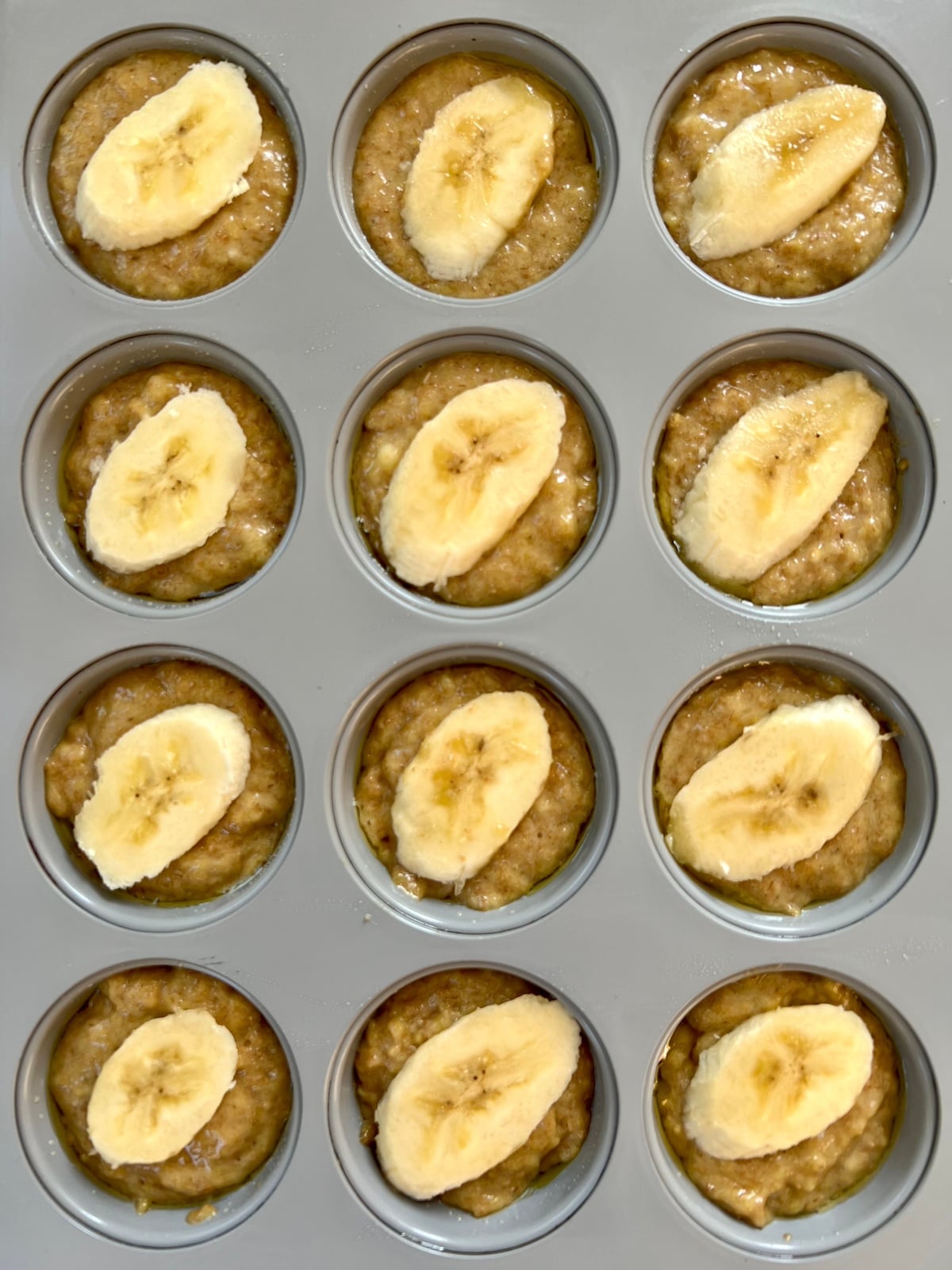 Wheat germ muffin batter in muffin tin. Each muffin topped with a slice of banana.