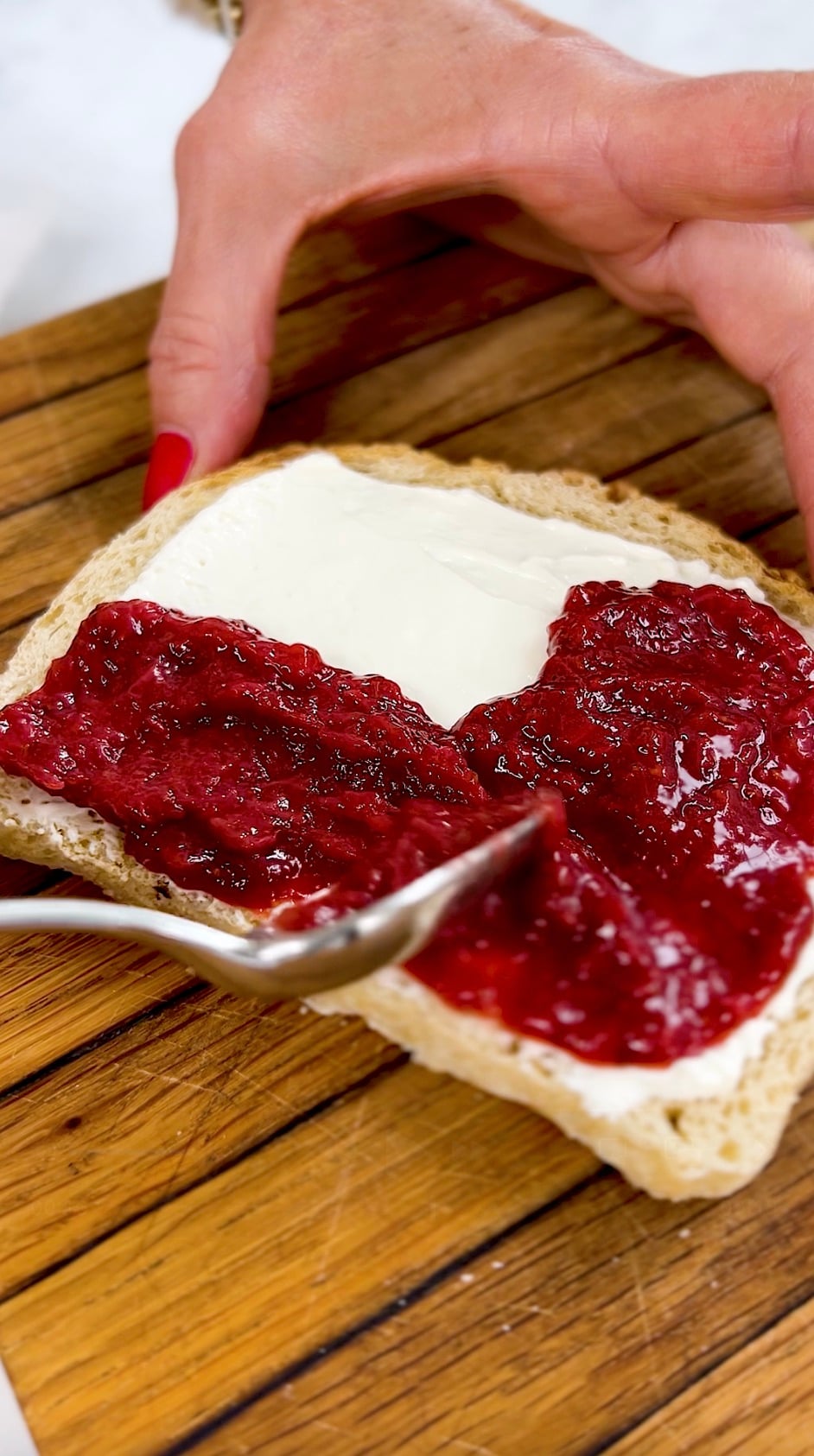 Spreading jam over cream cheese on a piece of toast.