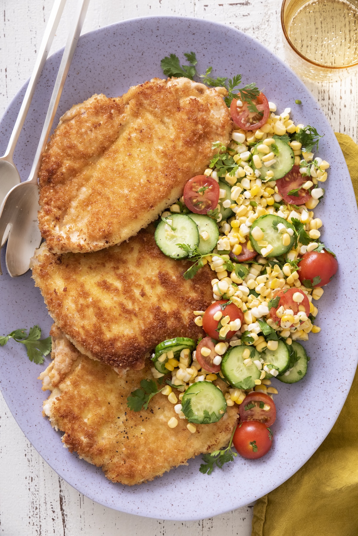 Three golden crispy chicken paillard cutlets on a platter with a fresh summer corn salad.