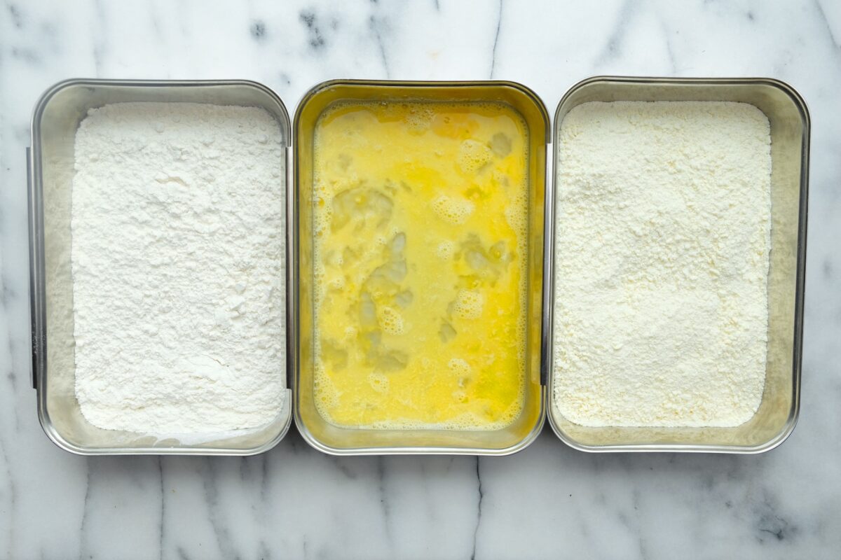 A breading station with three dishes of flour, whisked eggs, and panko bread crumbs.