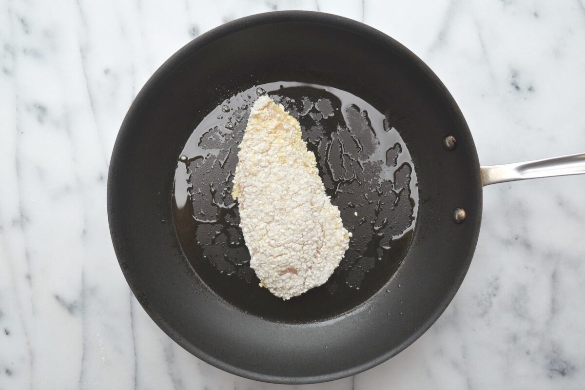 A panko-breaded chicken paillard frying in oil in a black skillet.