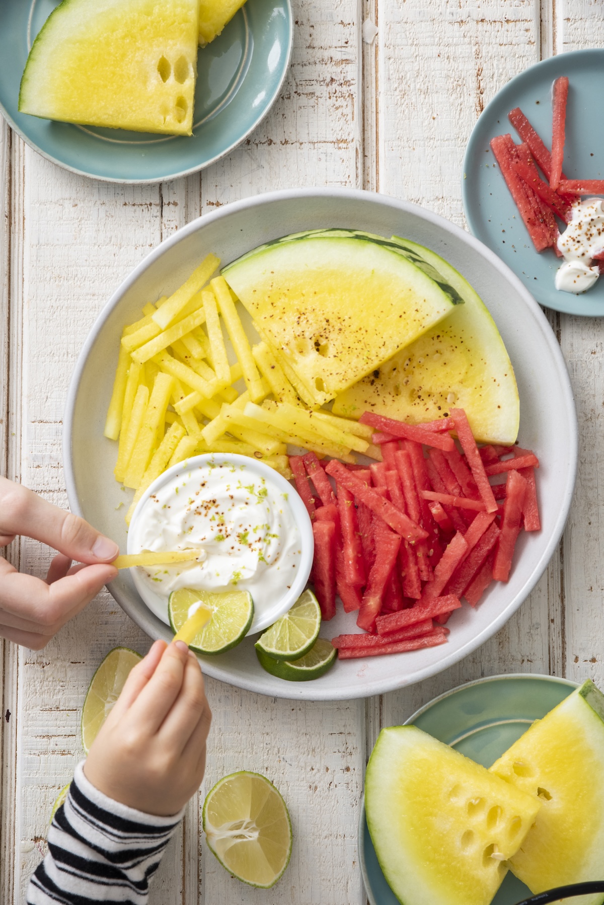 Hands dipping watermelon fries in yogurt dip.