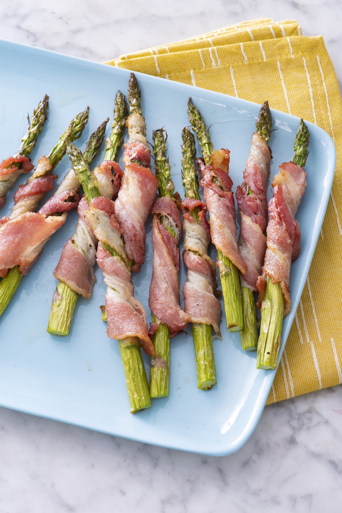 air fryer bacon wrapped asparagus on a blue serving platter.