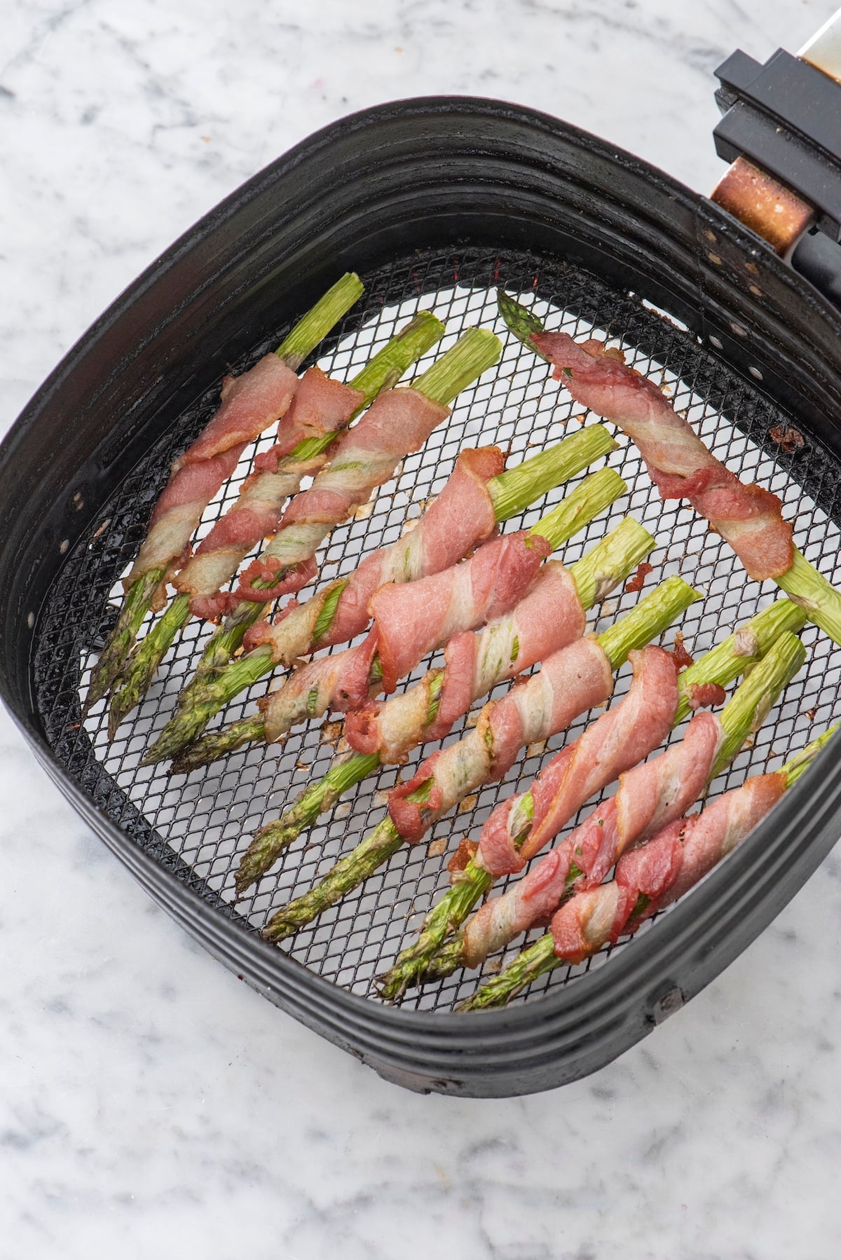 cooked bacon wrapped asparagus in air fryer basket.