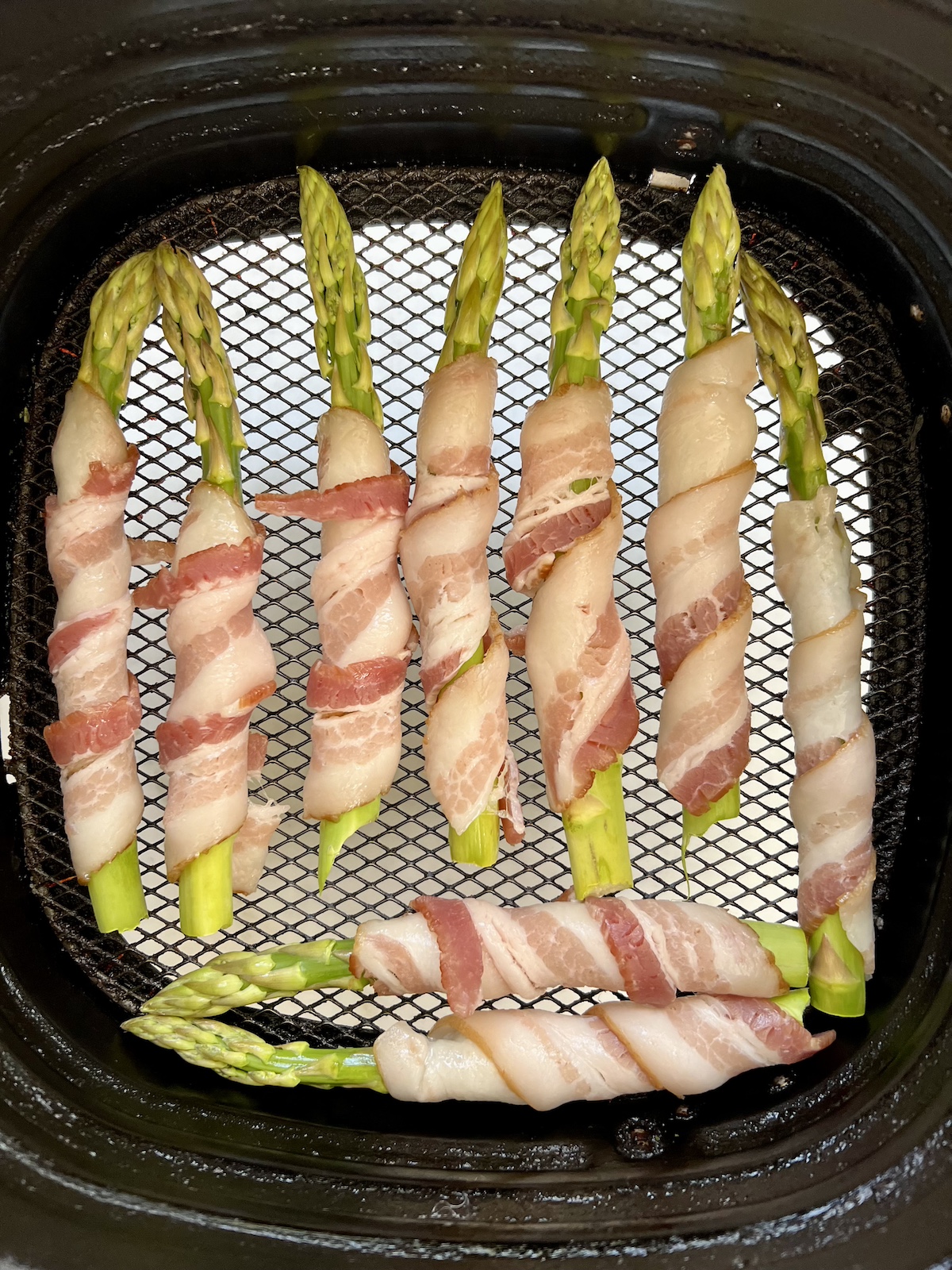uncooked bacon wrapped asparagus in air fryer basket.