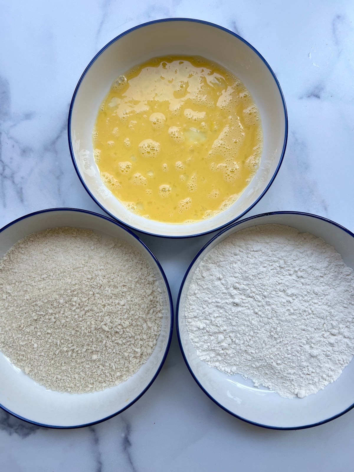 Three bowls. One with panko, one with whisked eggs, and the third with flour.