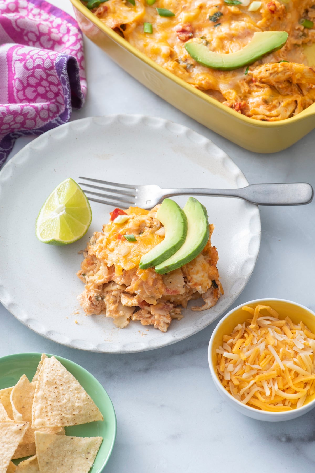 A serving of Mexican lasagna on a plate next to the casserole dish.