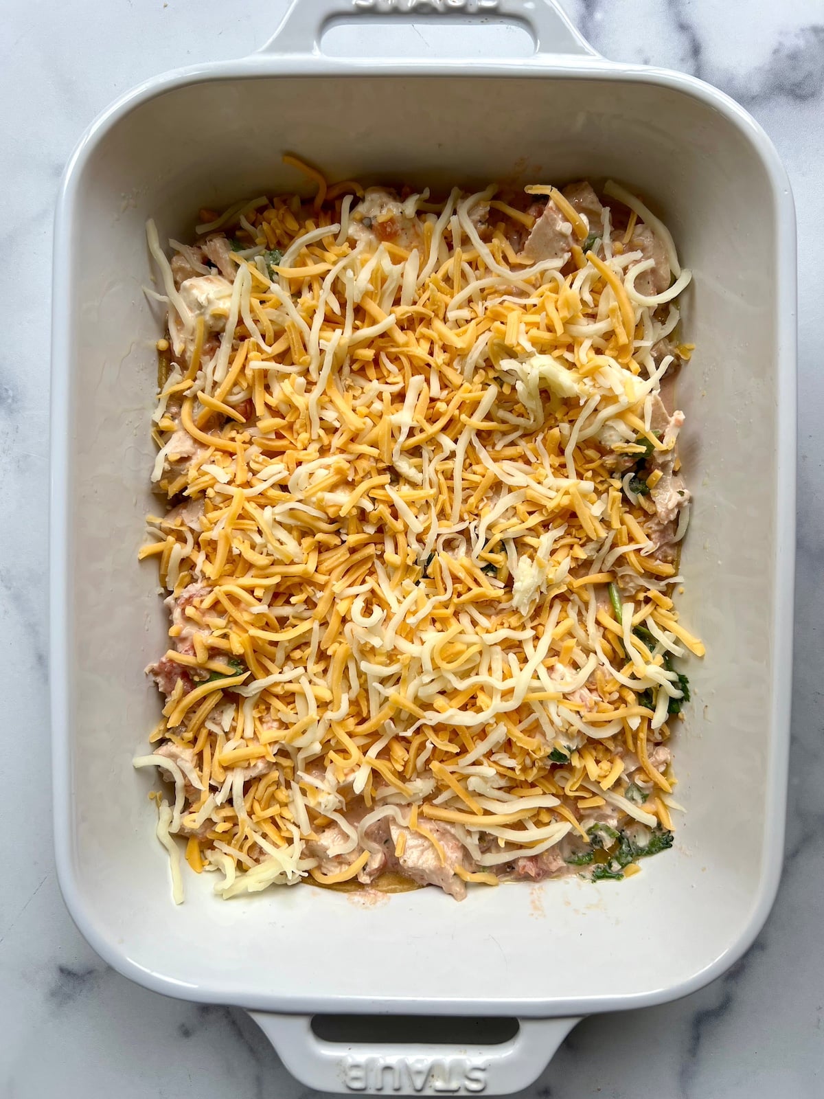 Tortillas, chicken mixture and shredded cheese layered in baking dish.
