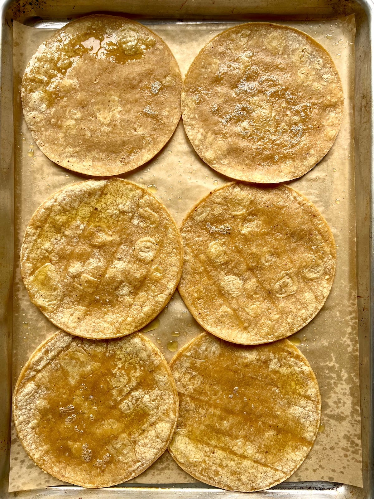 Tortillas spritzed with cooking oil on a baking sheet.