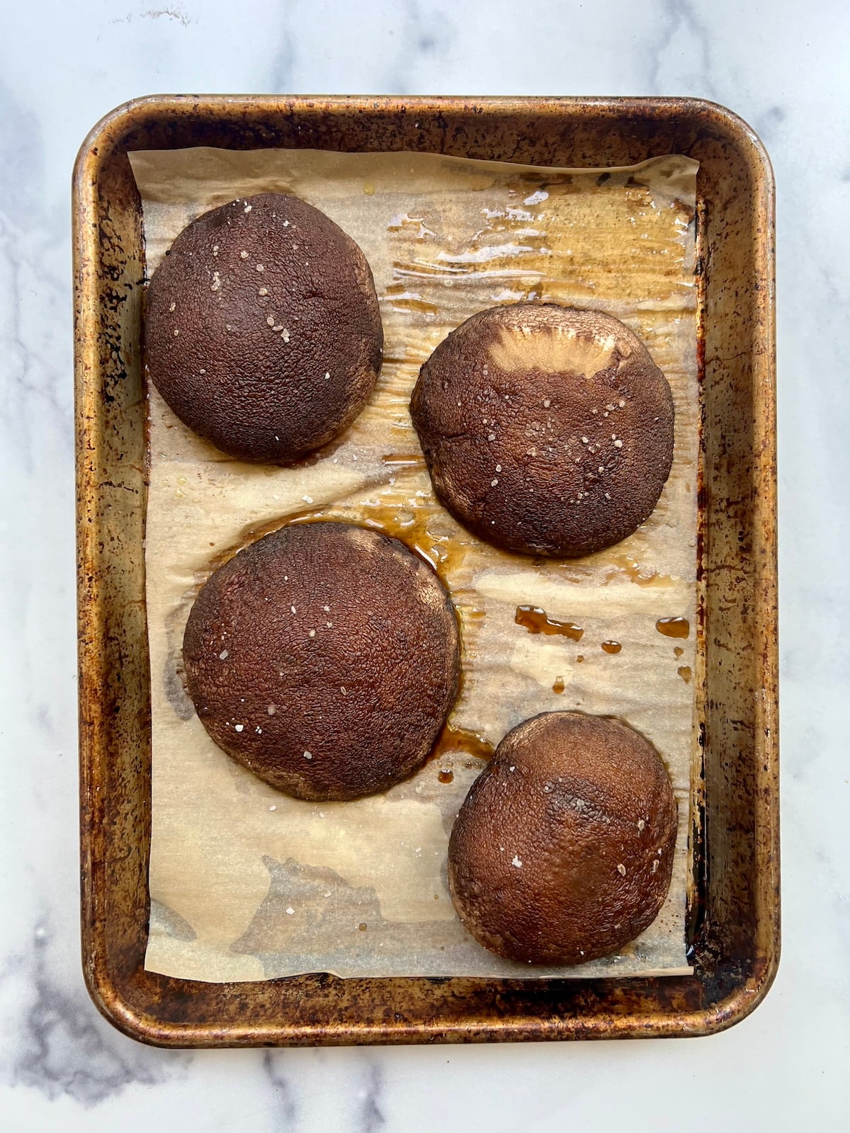 Four portobello mushrooms on baking sheet.