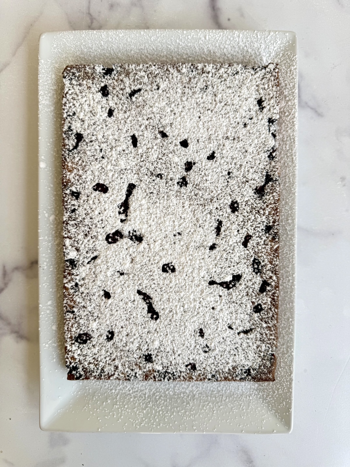 Blackberry tea cake dusted with powdered sugar on a white serving platter.