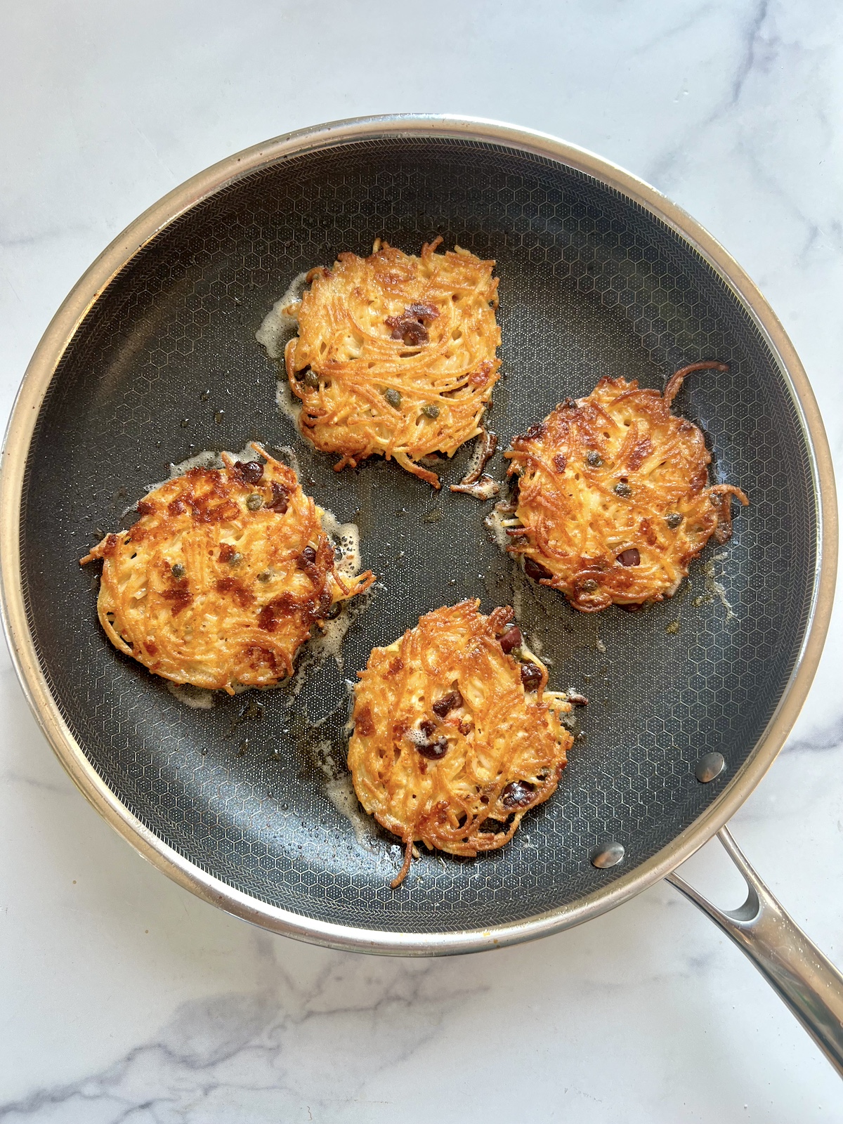 Cooked spaghetti cakes in sauté pan.