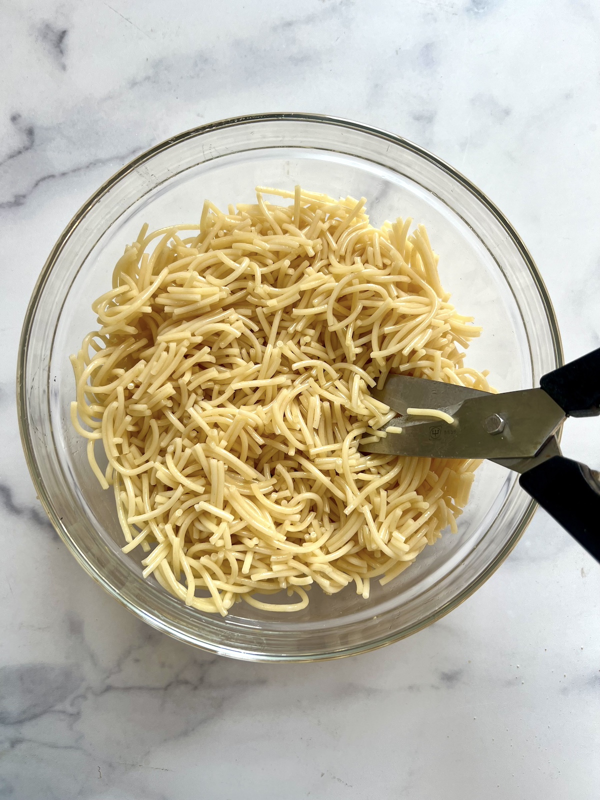 Spaghetti noodles in a bowl being cut with kitchen shears.