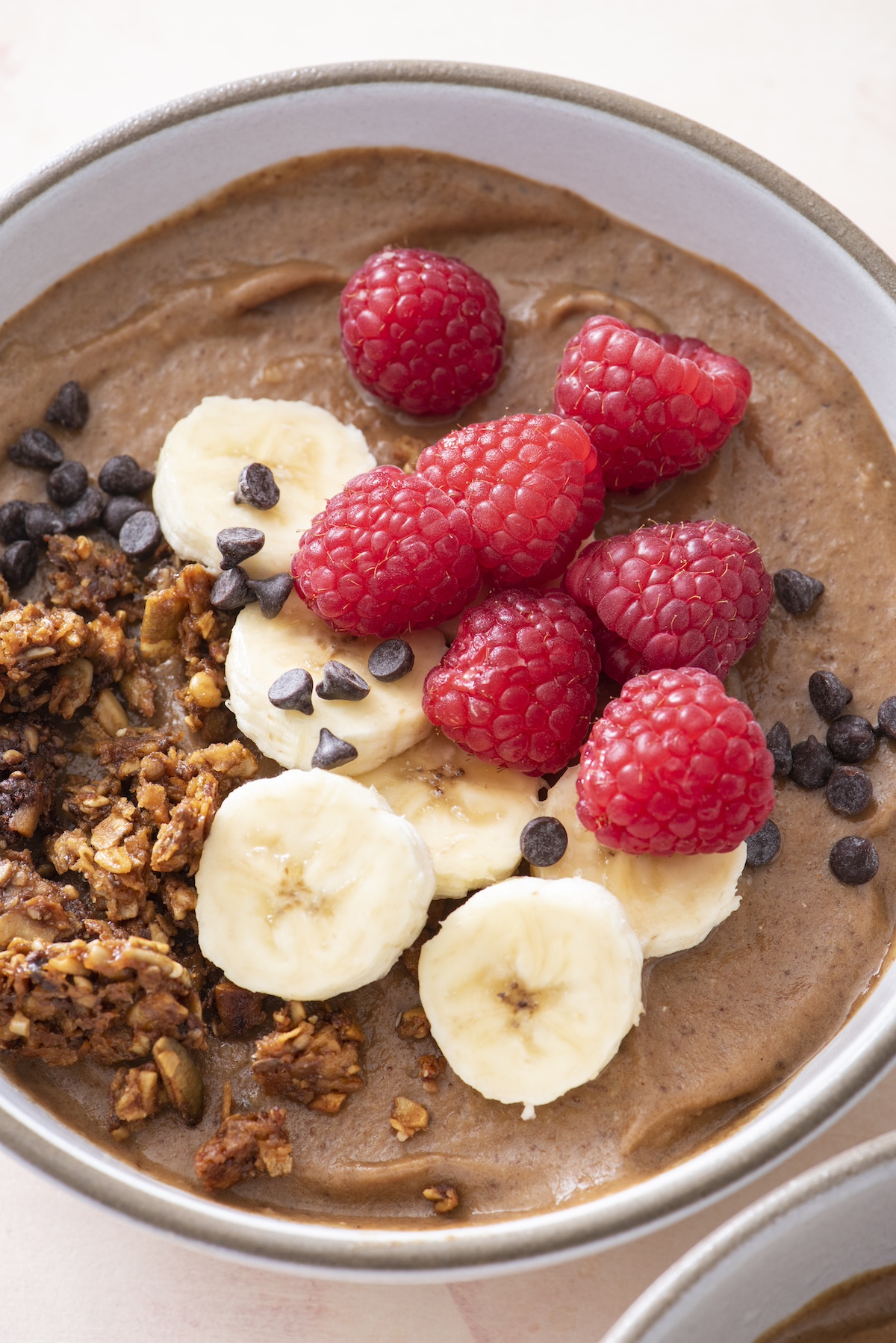 Double chocolate smoothie bowl topped with chocolate chips, granola, raspberries and bananas.