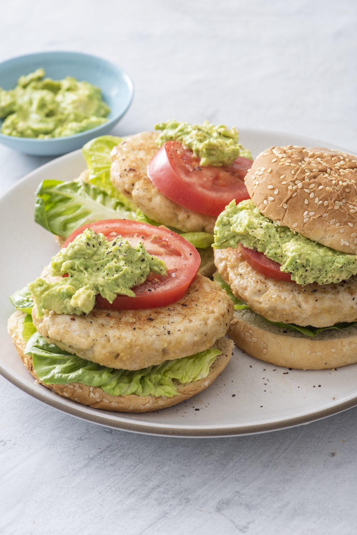 Juicy turkey burgers with oats served on sesame buns with guacamole, tomato, and lettuce on a white plate.