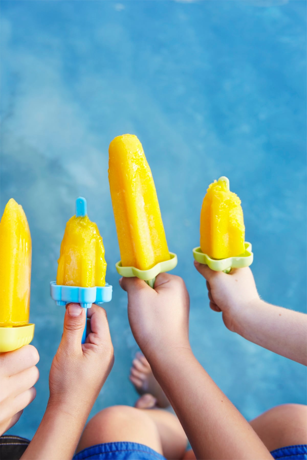 Hands holding mango popsicles.