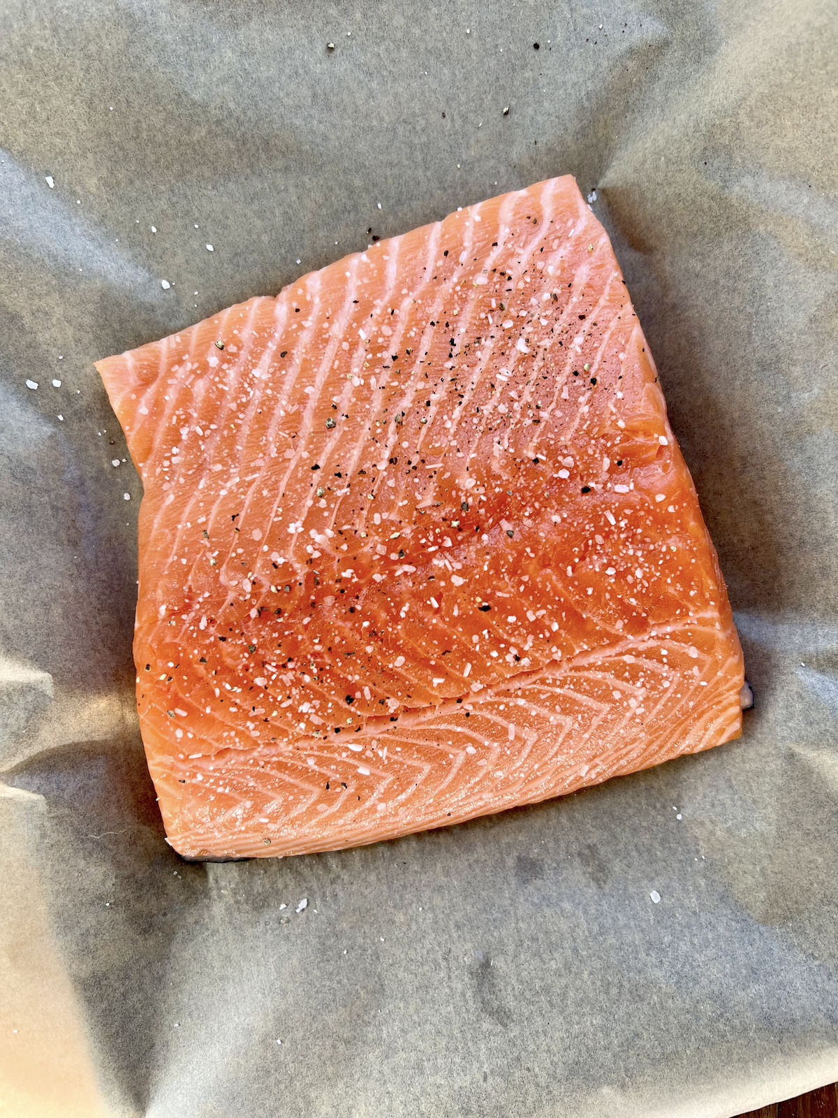 Piece of salmon with salt and pepper on parchment lined baking sheet.