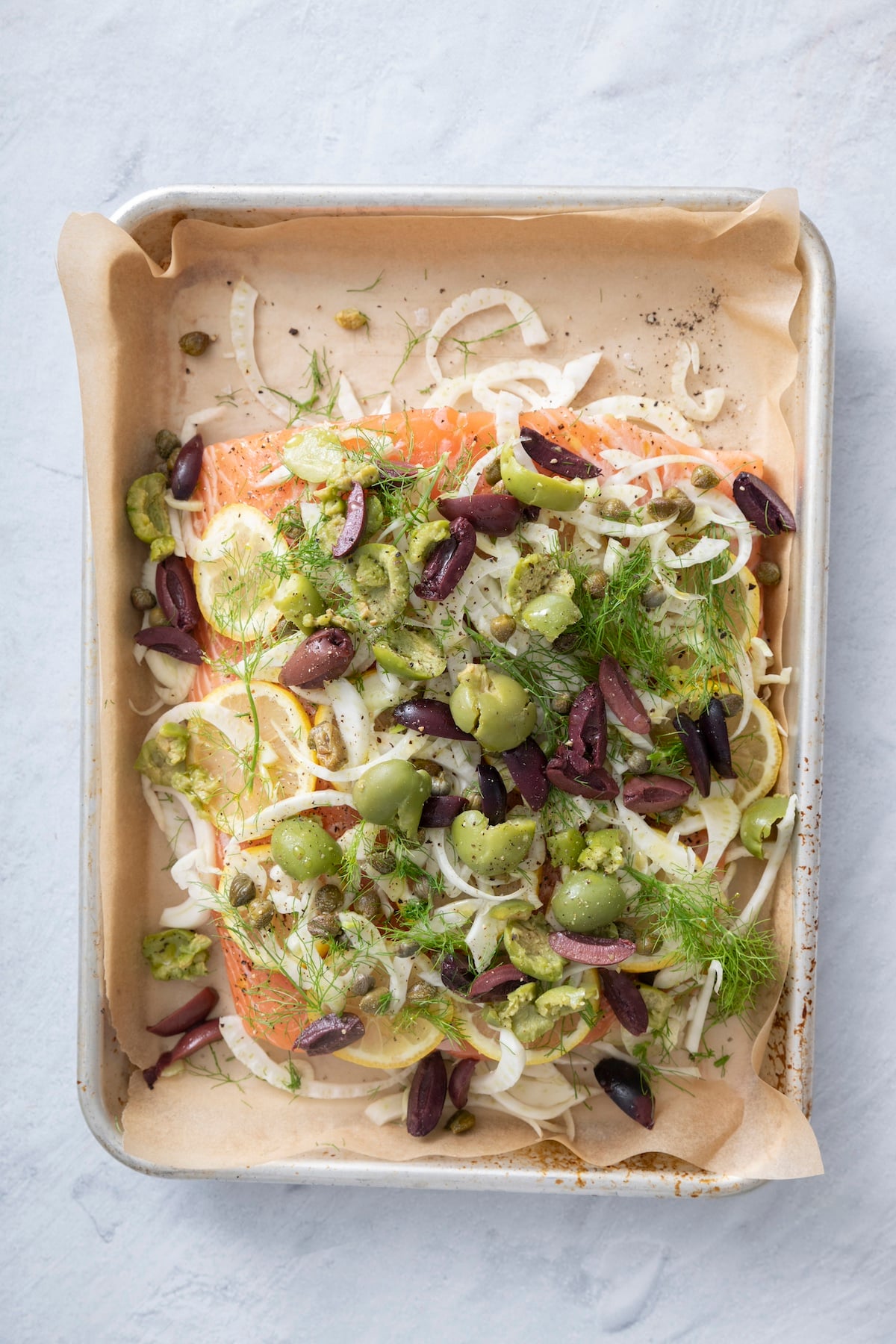 Salmon topped with fennel, lemons, olives and capers ready to be baked.