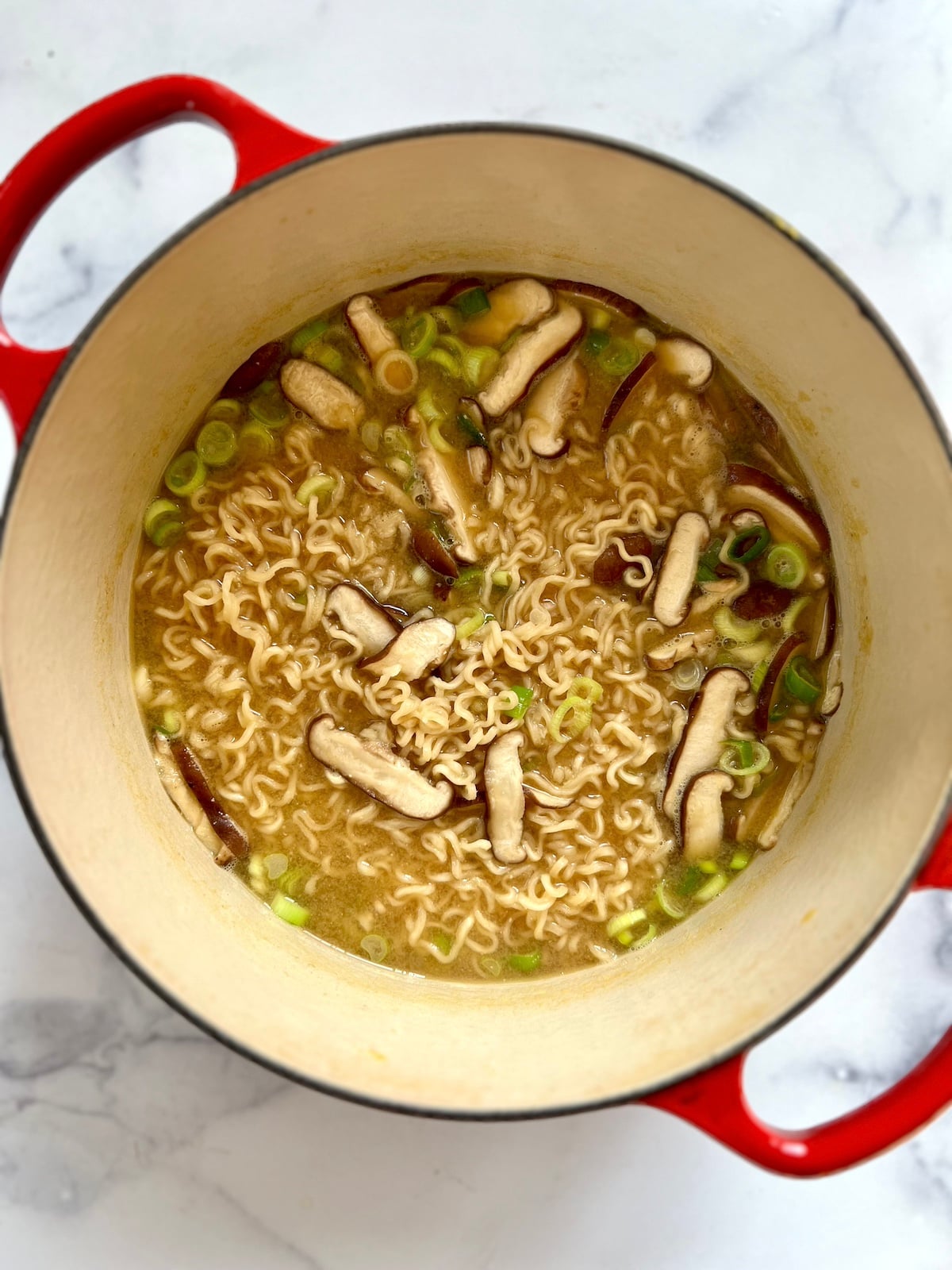Ramen noodle soup with shiitake mushroom and scallions in large sauce pan.