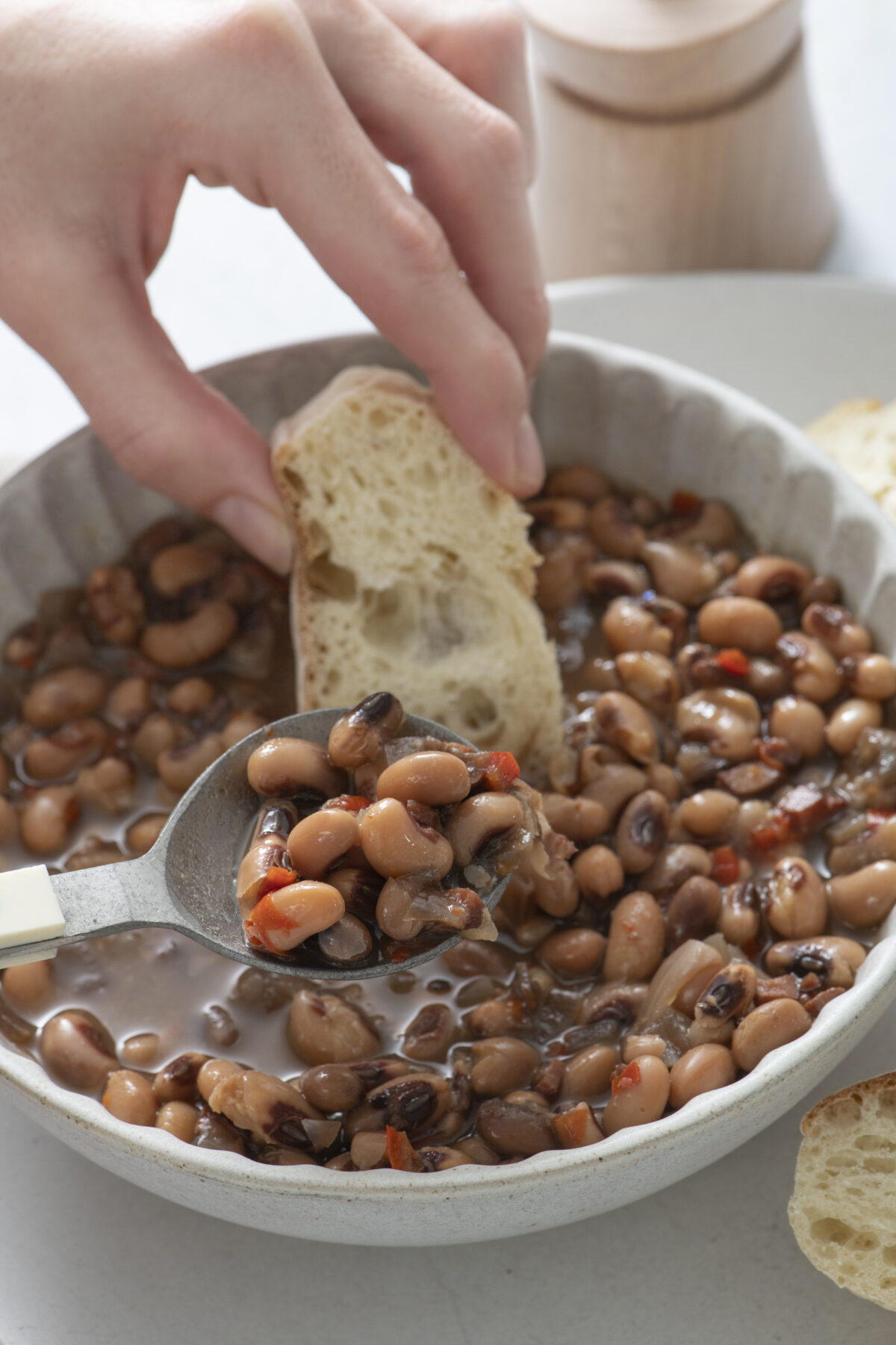 Hand dipping a piece of bread in black eyed peas.