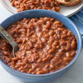 Baked beans in a blue bowl with a spoon.