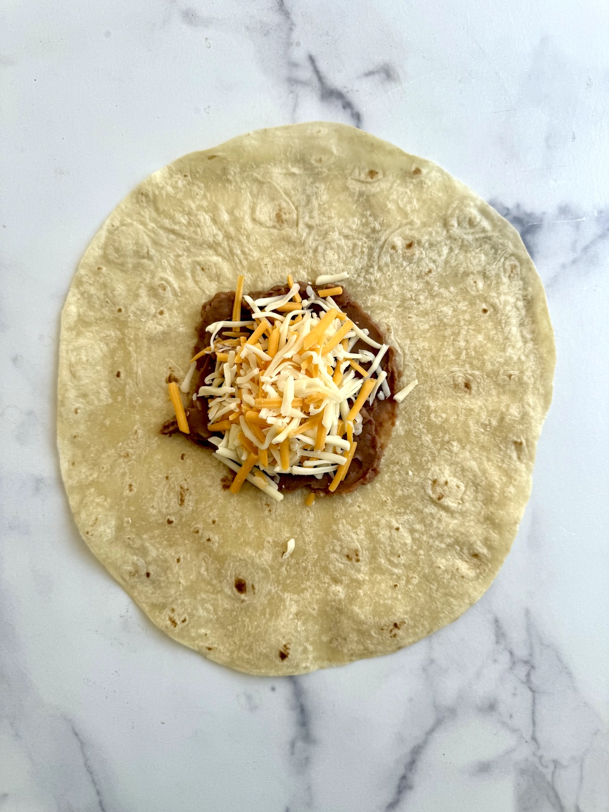 Refried beans and shredded cheese on top of a tortilla.