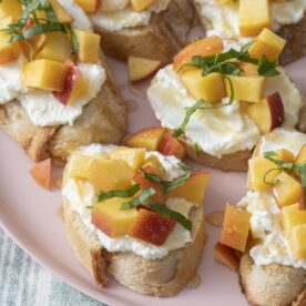Peach and ricotta crostini on pink plate.