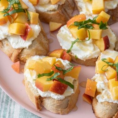 Peach and ricotta crostini on pink plate.