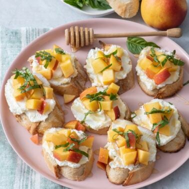 Peach and ricotta crostinis on a pink serving plate.