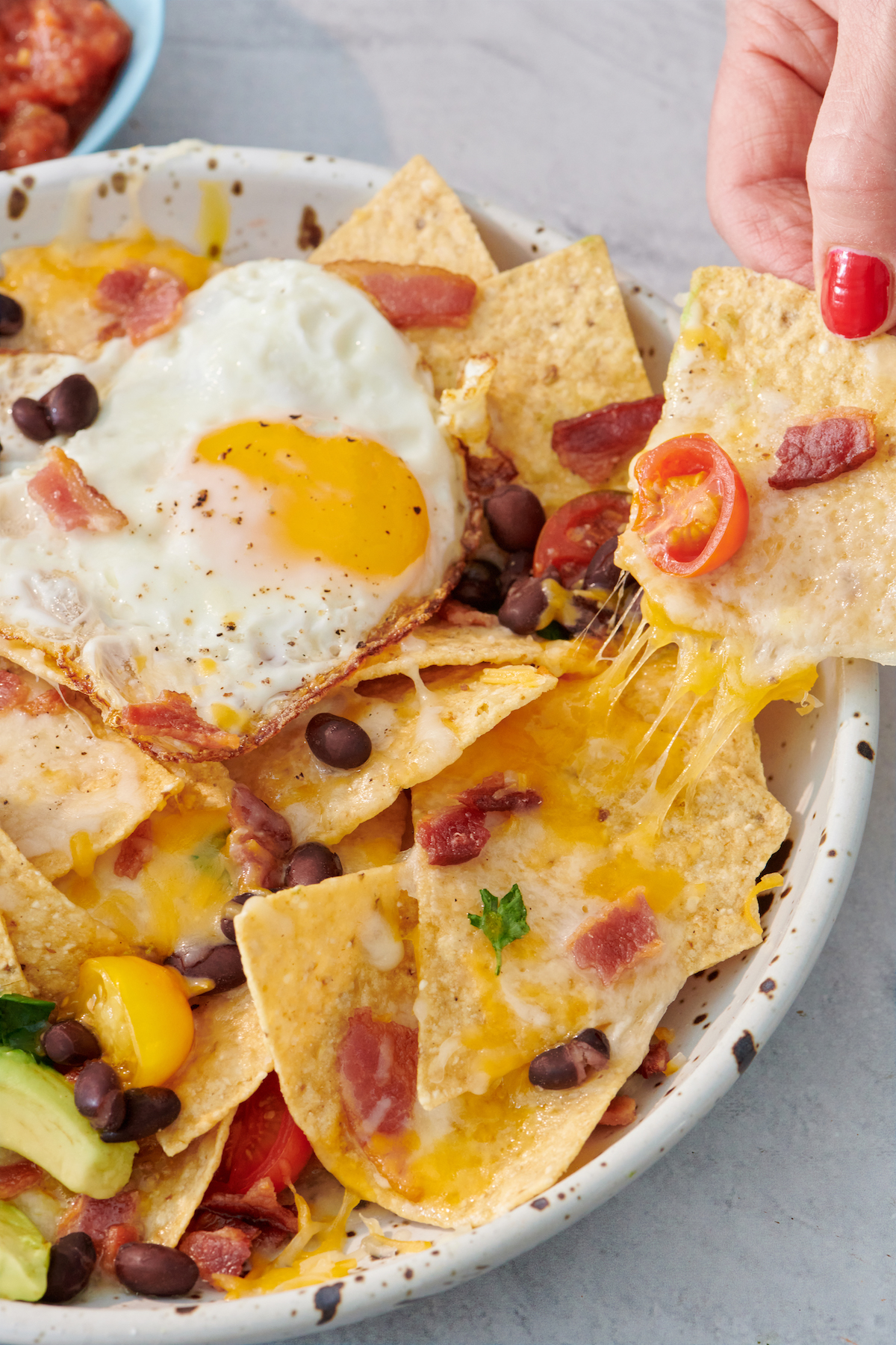 pulling a chip from serving of breakfast nachos topped with fried egg