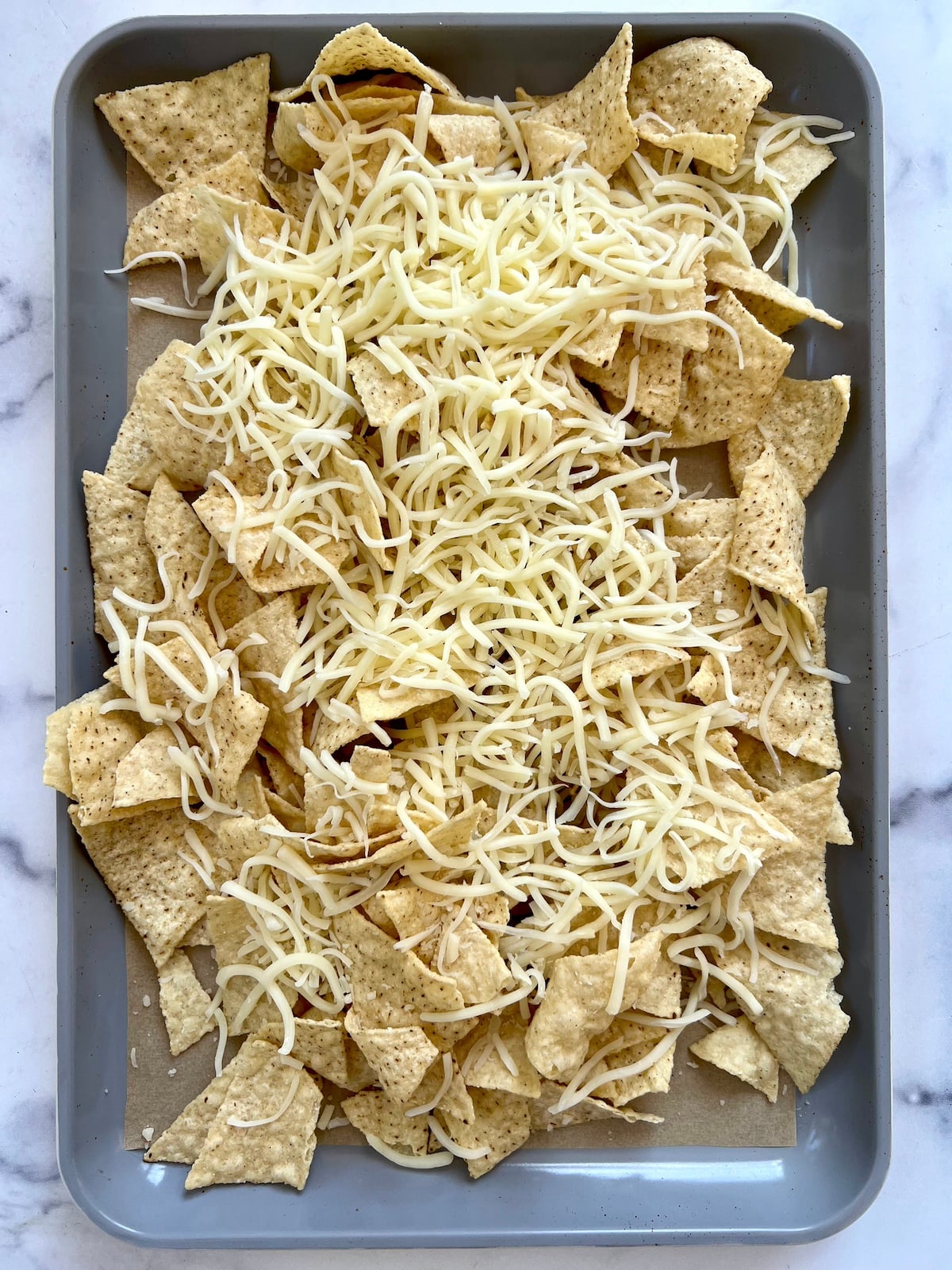 Tortilla chips on baking sheet topped with shredded cheese.