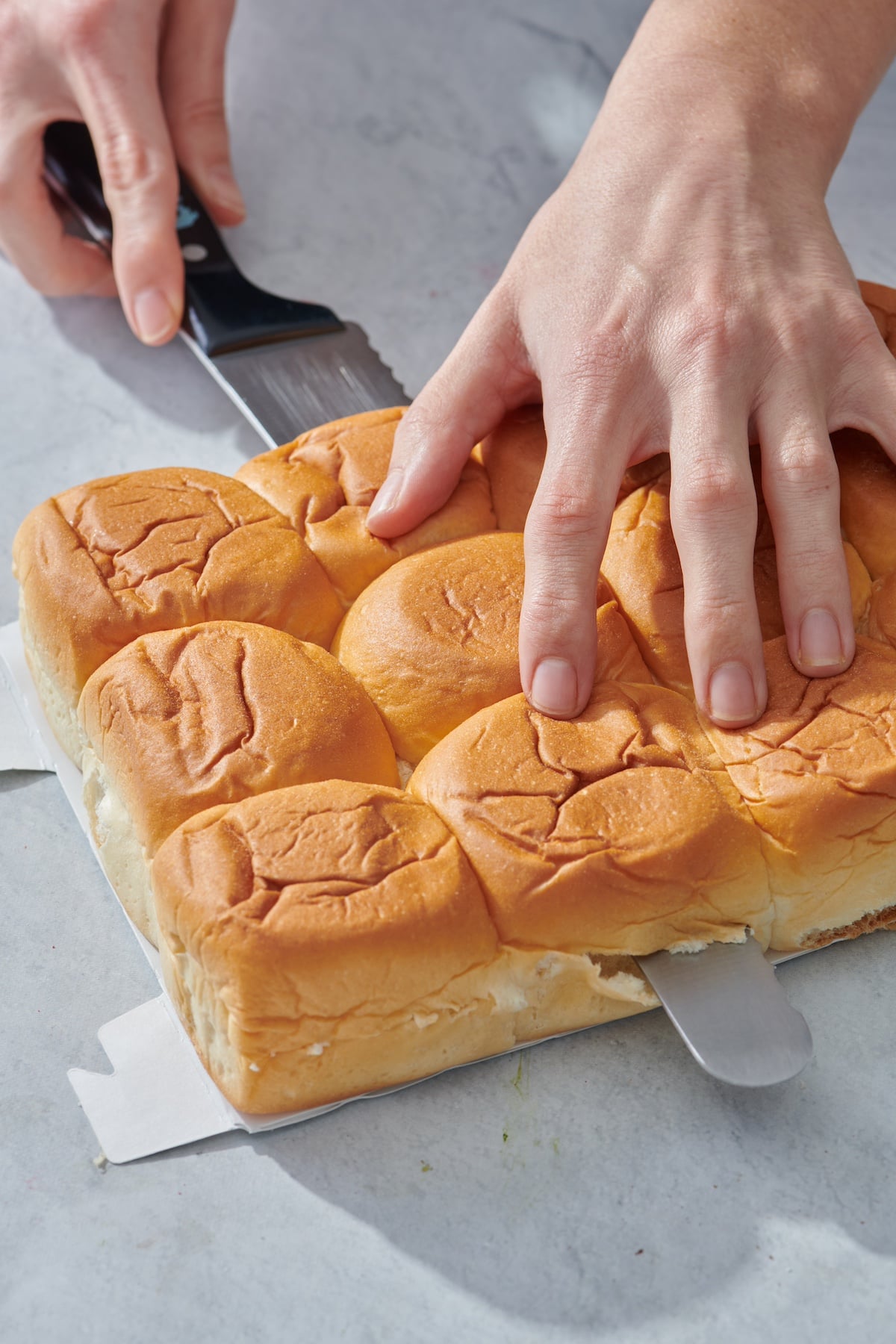 Cutting Hawaiian rolls in half, lengthwise.