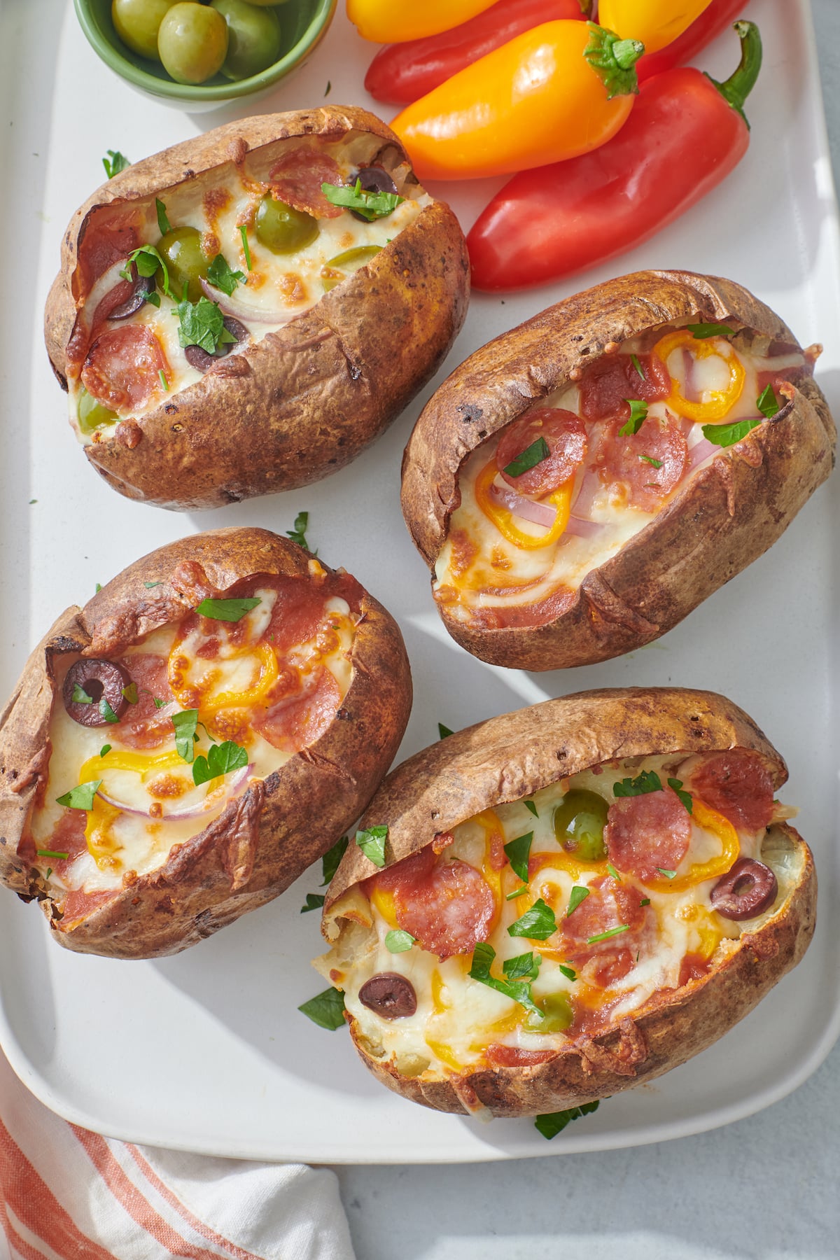 Four pizza stuffed potatoes on a platter with mini peppers.