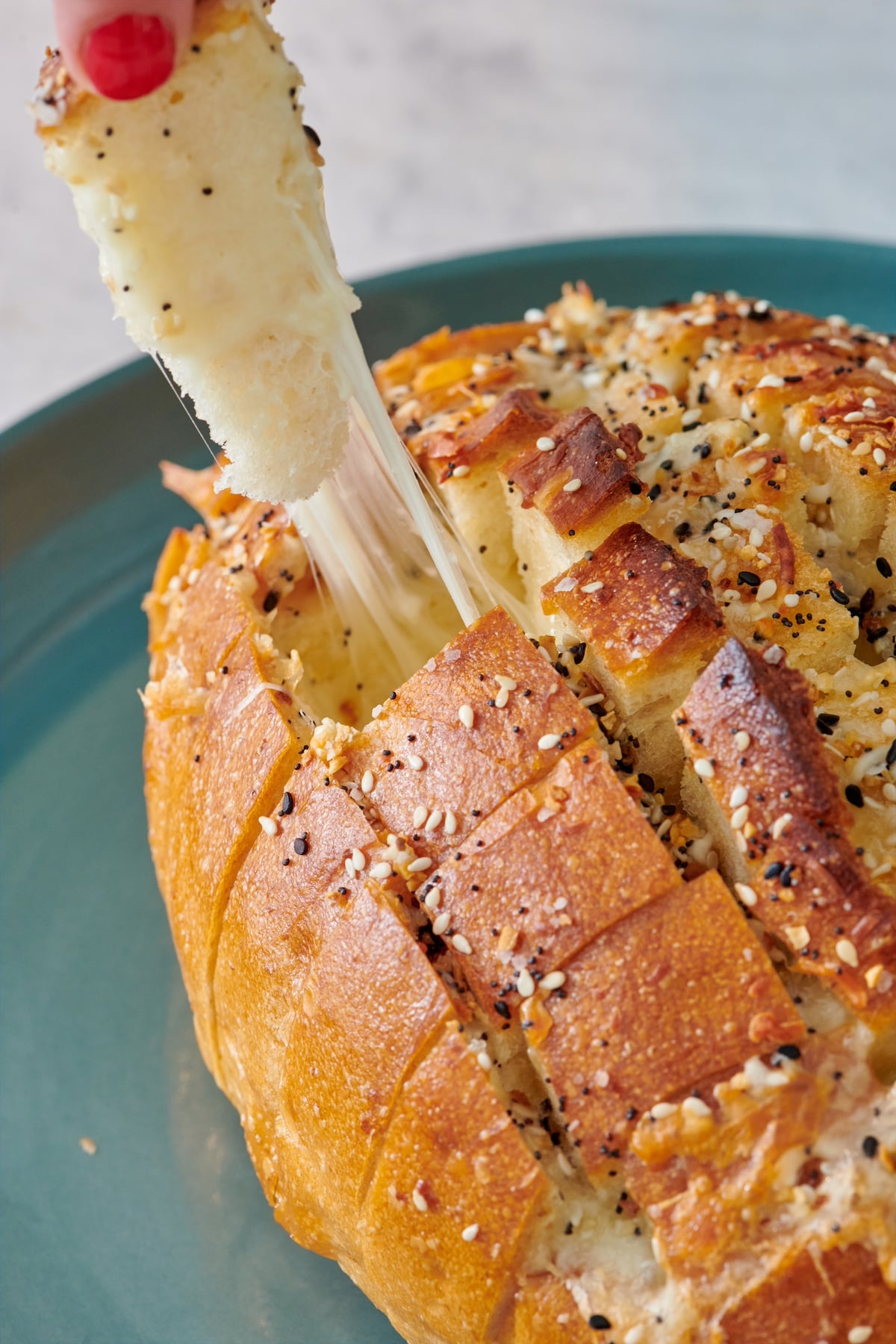Hand grabbing a piece of cheese bread from the loaf.