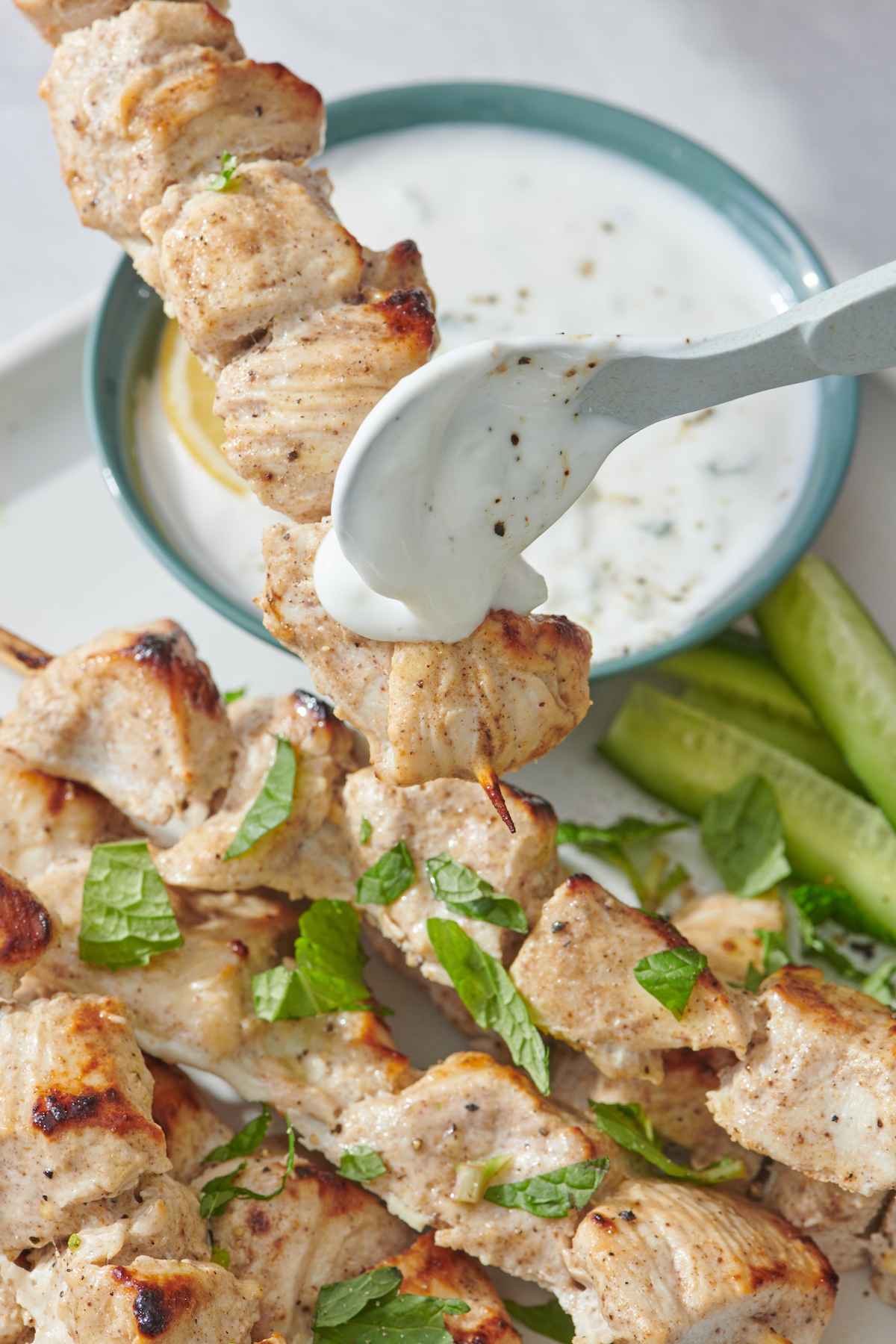 Chicken tikka skewer dipping in cucumber mint raita.