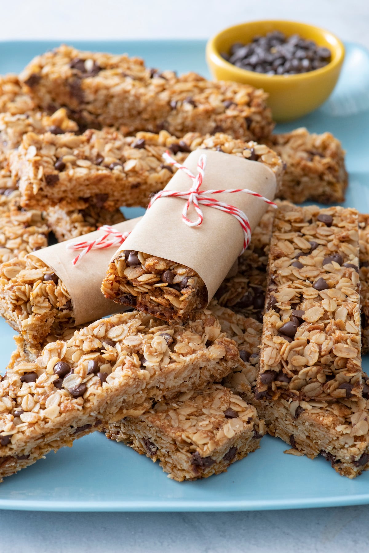 Two homemade chocolate chip granola bars wrapped in parchment on top of unwrapped bars.
